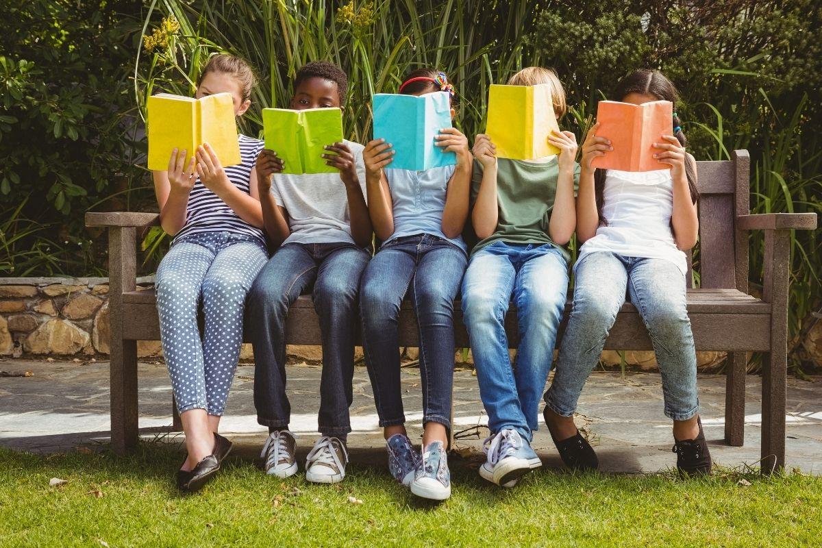 Five children sitting on a bench enjoying reading books.